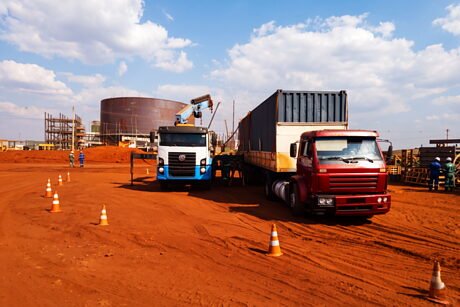 Movimentação de um contêiner entre veículos no pátio de uma unidade industrial.